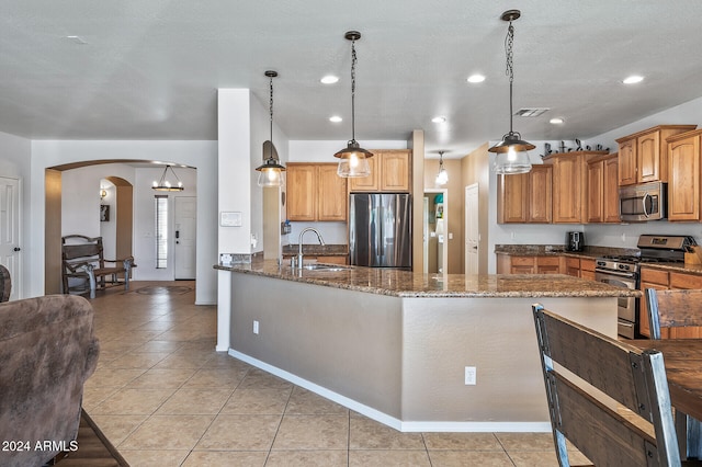 kitchen featuring stainless steel appliances, dark stone counters, sink, light tile patterned flooring, and decorative light fixtures