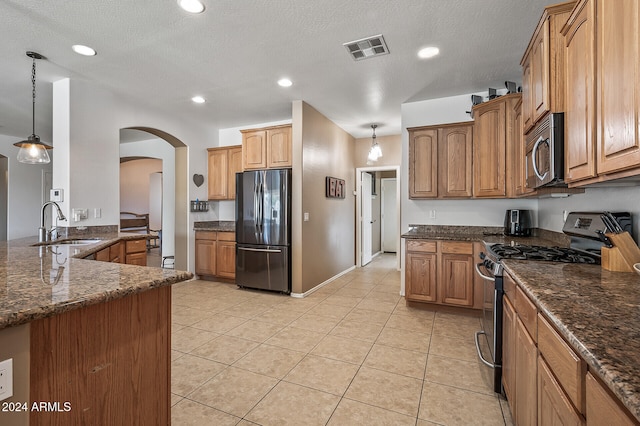 kitchen with appliances with stainless steel finishes, a textured ceiling, dark stone counters, and pendant lighting