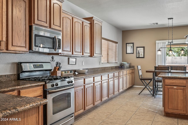 kitchen featuring appliances with stainless steel finishes, hanging light fixtures, a textured ceiling, and light tile patterned floors