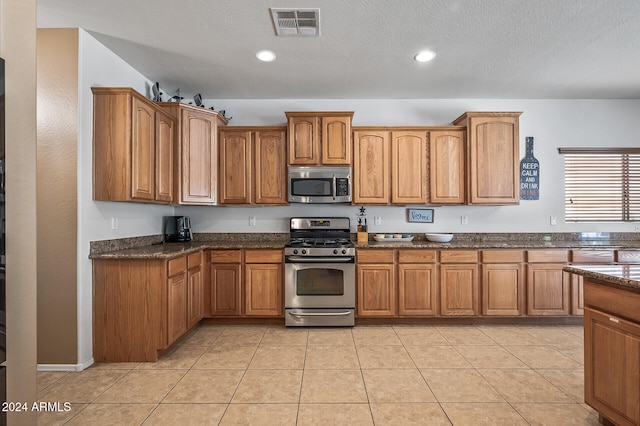 kitchen featuring stainless steel appliances, a textured ceiling, light tile patterned floors, and dark stone counters