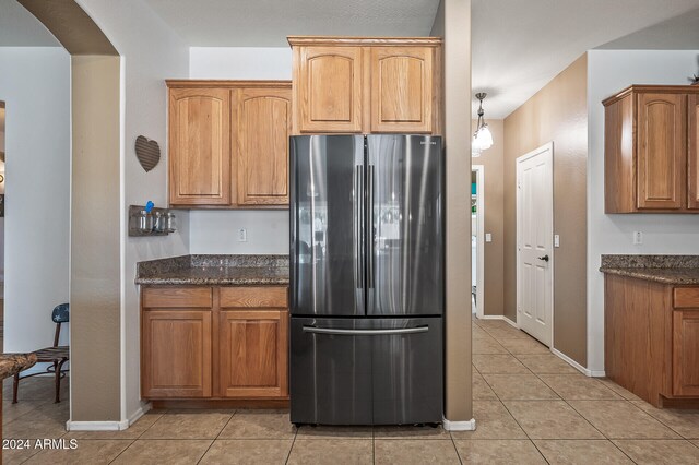 kitchen with dark stone counters, pendant lighting, light tile patterned floors, and stainless steel refrigerator