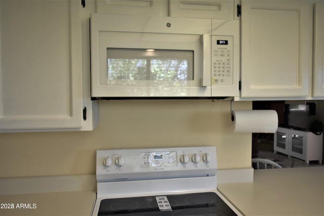 kitchen featuring electric range oven, light countertops, white microwave, and white cabinetry