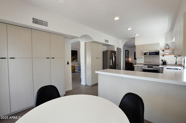 kitchen featuring sink, kitchen peninsula, cream cabinetry, stainless steel appliances, and backsplash