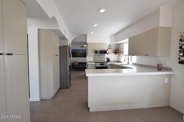 kitchen with sink, stainless steel appliances, cream cabinets, light tile patterned flooring, and kitchen peninsula