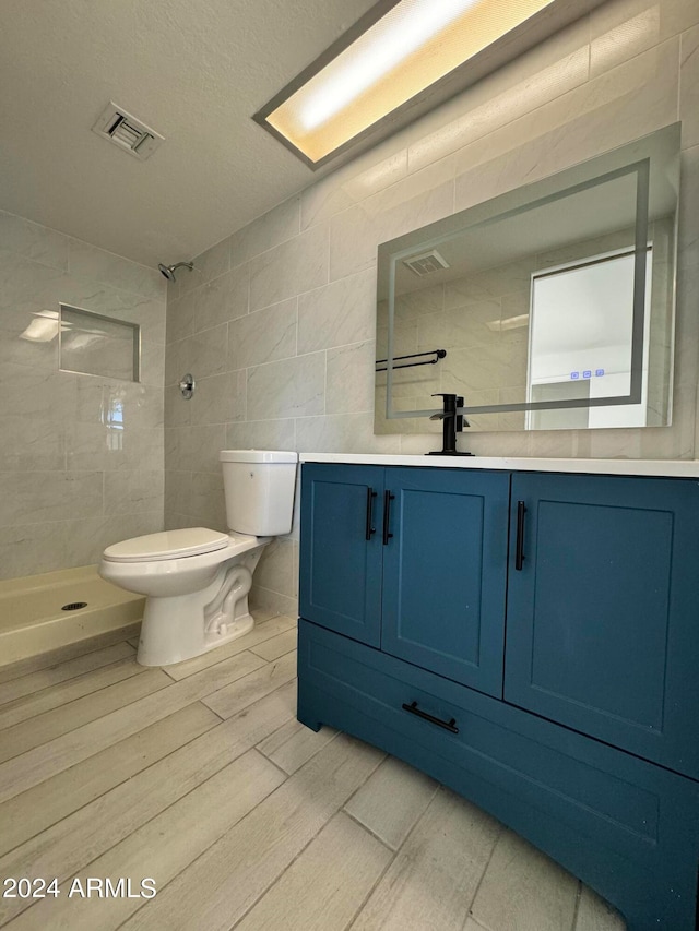 bathroom with tile flooring, tile walls, toilet, vanity, and a tile shower