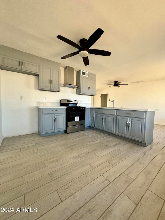 kitchen with stainless steel range oven, ceiling fan, gray cabinetry, light hardwood / wood-style floors, and wall chimney range hood