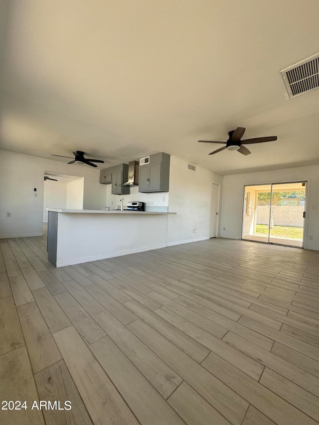 interior space featuring gray cabinets, light hardwood / wood-style floors, ceiling fan, and wall chimney exhaust hood