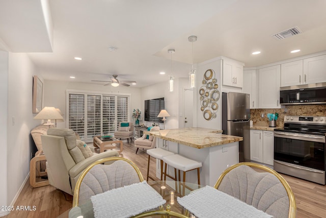 kitchen with light stone countertops, white cabinets, stainless steel appliances, decorative backsplash, and hanging light fixtures