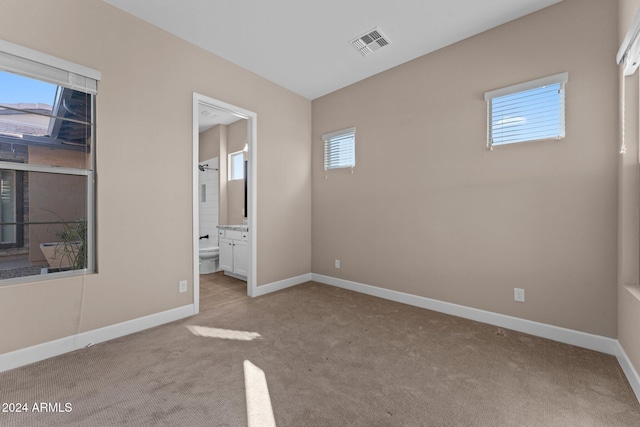 unfurnished bedroom featuring ensuite bathroom, light carpet, and multiple windows