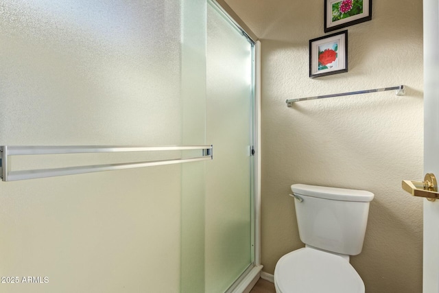 bathroom featuring a shower with door and toilet