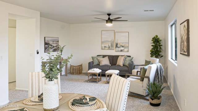 living area featuring baseboards, visible vents, a ceiling fan, and light colored carpet