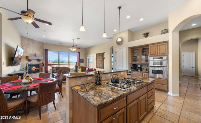 28309 N 156th Way, Scottsdale, AZ 85262 - kitchen with stainless steel appliances, a ceiling fan, arched walkways, brown cabinetry, and a large fireplace