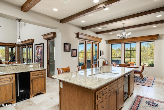 kitchen featuring beamed ceiling, hanging light fixtures, sink, a center island with sink, and black refrigerator