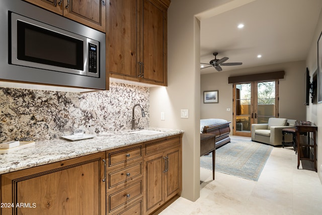 kitchen with ceiling fan, sink, backsplash, light stone countertops, and stainless steel microwave