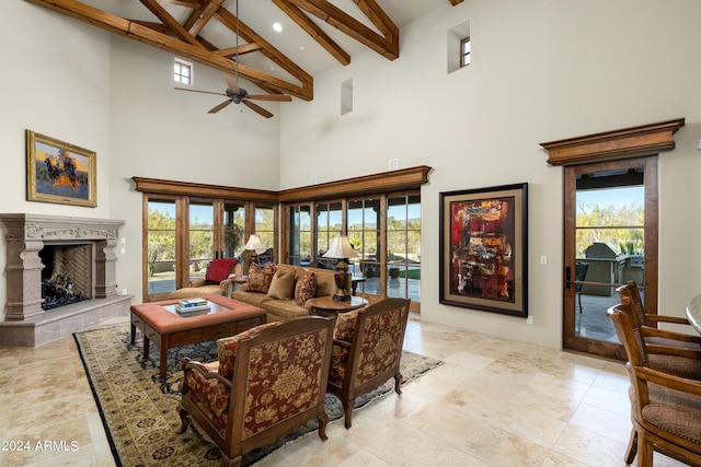 living room with a high ceiling, a tiled fireplace, ceiling fan, and beamed ceiling