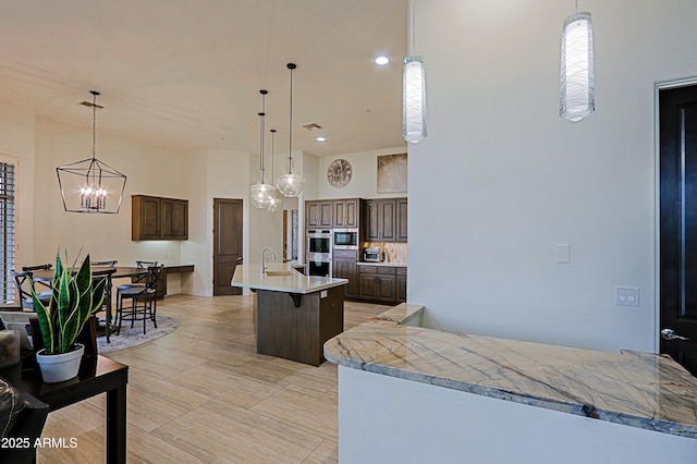 kitchen with an island with sink, stainless steel appliances, light countertops, dark brown cabinets, and hanging light fixtures