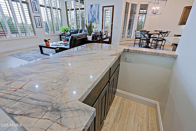 kitchen with baseboards, light stone counters, light wood-style flooring, an inviting chandelier, and hanging light fixtures