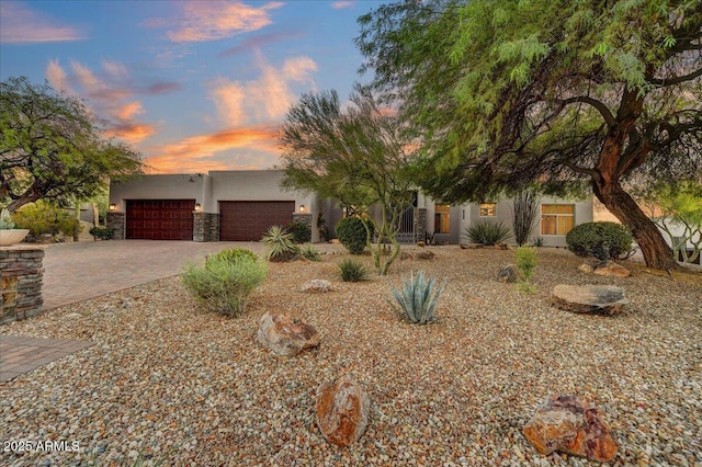 view of front of property featuring stone siding, stucco siding, decorative driveway, and a garage