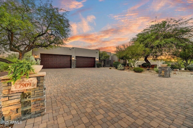 pueblo-style house with stucco siding, decorative driveway, and an attached garage