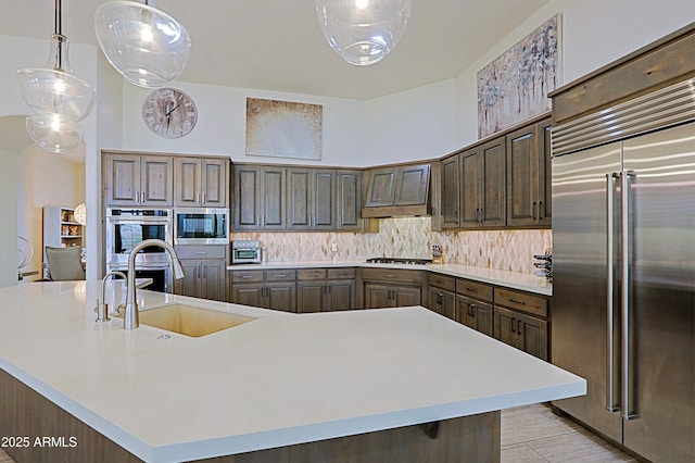 kitchen with premium range hood, a sink, light countertops, decorative backsplash, and built in appliances