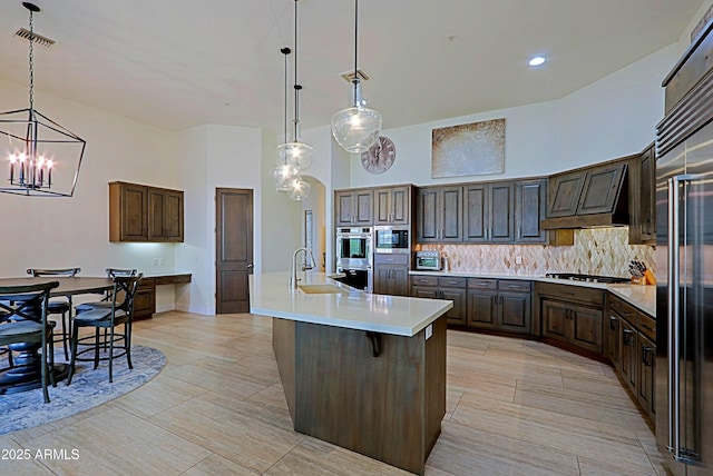 kitchen featuring a sink, a high ceiling, dark brown cabinetry, light countertops, and decorative backsplash