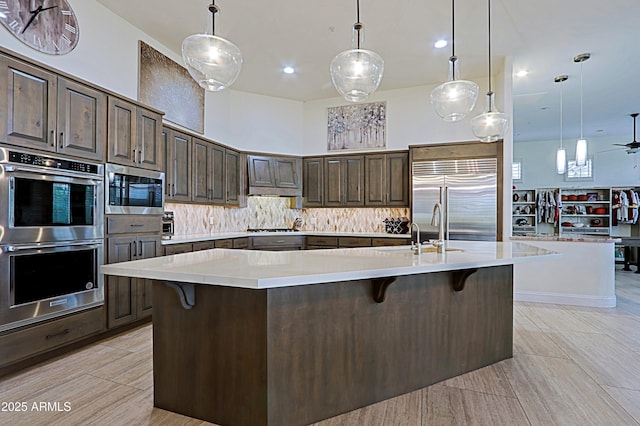 kitchen featuring tasteful backsplash, built in appliances, a kitchen bar, light countertops, and a sink