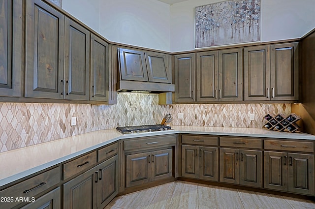 kitchen featuring tasteful backsplash, dark brown cabinets, under cabinet range hood, light countertops, and stainless steel gas stovetop