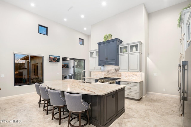 kitchen with light stone countertops, a towering ceiling, a kitchen island with sink, sink, and white cabinetry