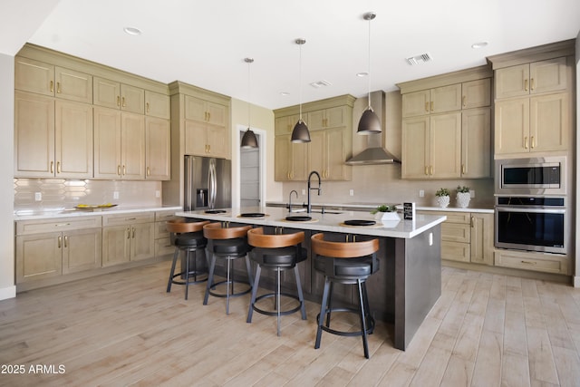 kitchen with light countertops, visible vents, appliances with stainless steel finishes, wall chimney range hood, and a kitchen breakfast bar