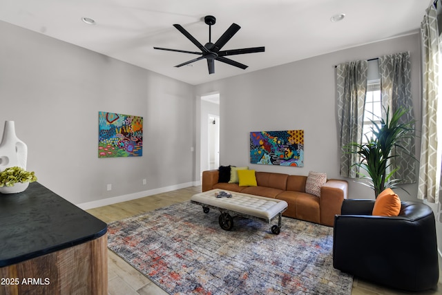 living room with a ceiling fan, light wood finished floors, and baseboards