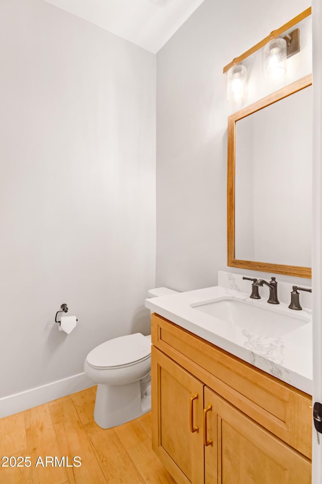 half bathroom featuring toilet, baseboards, wood finished floors, and vanity