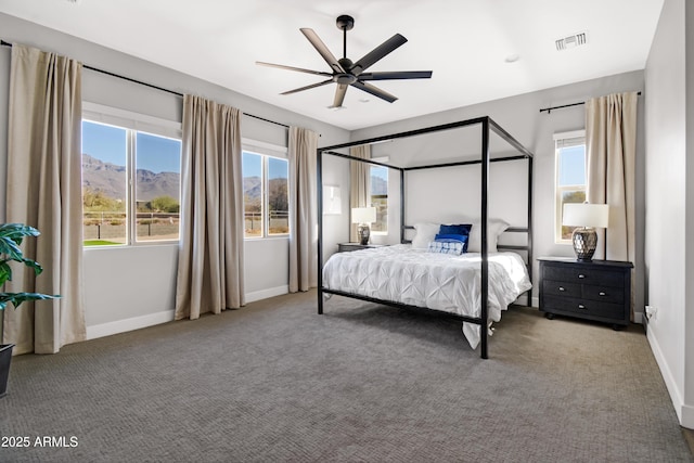 carpeted bedroom featuring a ceiling fan, multiple windows, visible vents, and baseboards