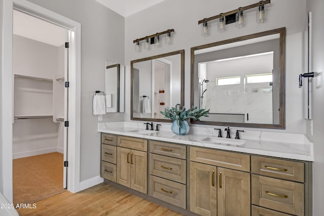 bathroom featuring double vanity, wood finished floors, a sink, and a walk in closet