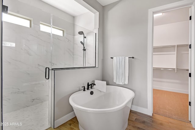 full bathroom featuring a freestanding bath, wood finished floors, a marble finish shower, and a walk in closet