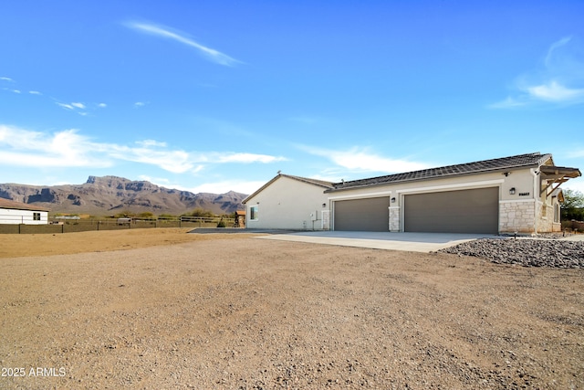 view of front of house with concrete driveway, an attached garage, fence, a mountain view, and stone siding