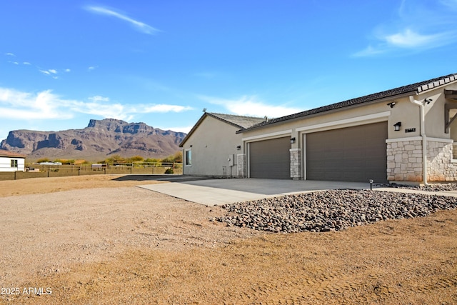 exterior space with stucco siding, concrete driveway, an attached garage, a mountain view, and fence