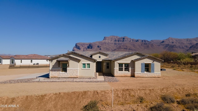 view of front facade featuring stone siding, a mountain view, and stucco siding