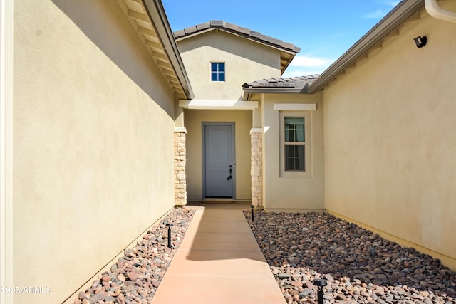 doorway to property featuring stone siding, a tile roof, and stucco siding