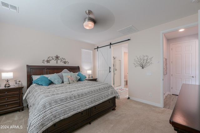 bedroom featuring ensuite bathroom, a barn door, light colored carpet, and ceiling fan