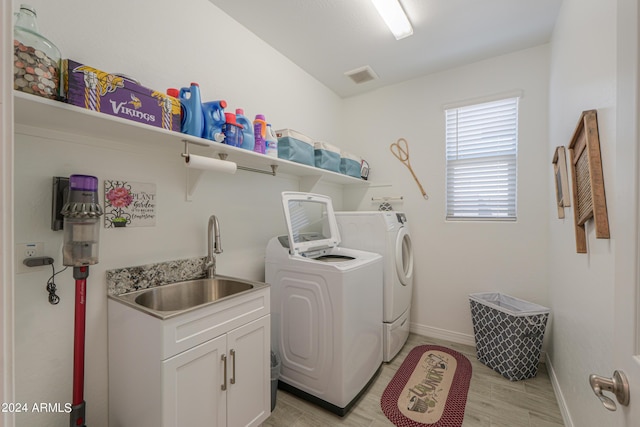 clothes washing area with light wood-type flooring, washer and clothes dryer, and sink