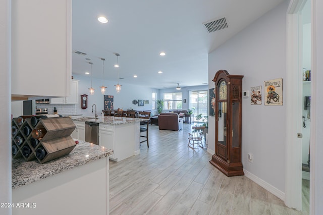 kitchen with pendant lighting, a breakfast bar, kitchen peninsula, stainless steel dishwasher, and white cabinetry