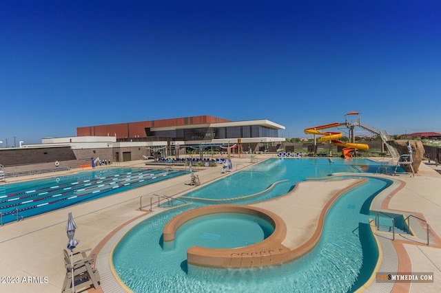 community pool with a water slide, a hot tub, and a patio