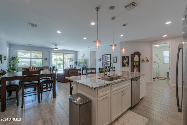 kitchen featuring white cabinetry, dishwasher, sink, light stone counters, and an island with sink