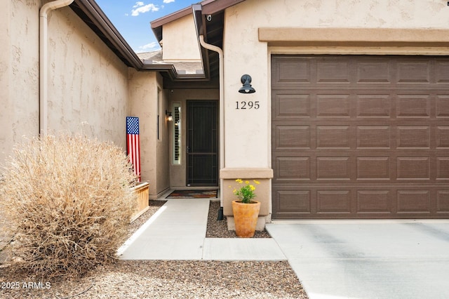 doorway to property featuring a garage, driveway, and stucco siding