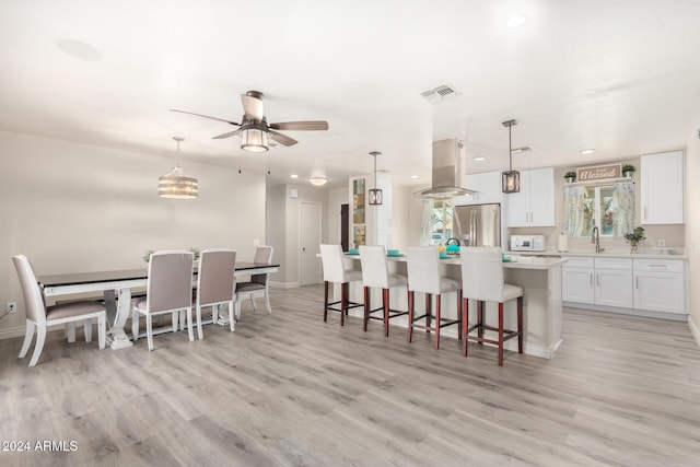 kitchen featuring decorative light fixtures, light hardwood / wood-style floors, white cabinetry, island exhaust hood, and stainless steel refrigerator