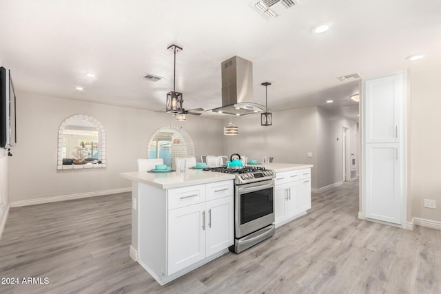 kitchen featuring hanging light fixtures, stainless steel gas range, ceiling fan, white cabinetry, and island exhaust hood