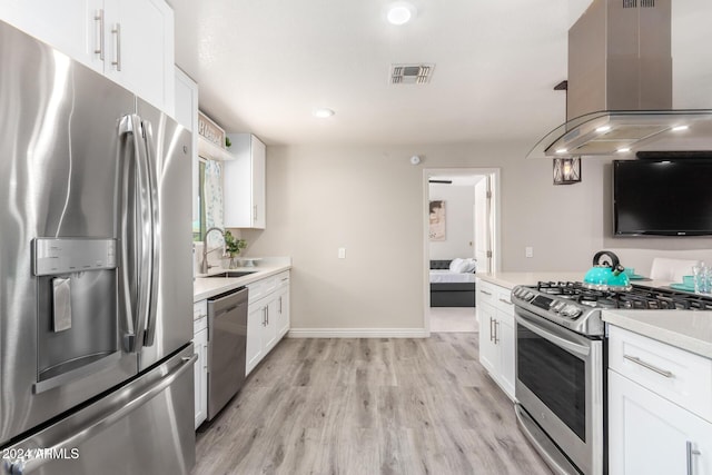 kitchen with white cabinets, island exhaust hood, appliances with stainless steel finishes, and light hardwood / wood-style flooring