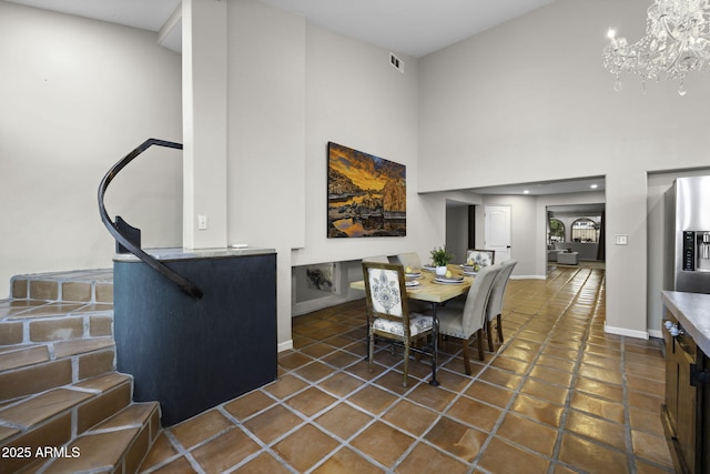 tiled dining space with a chandelier, baseboards, and a towering ceiling