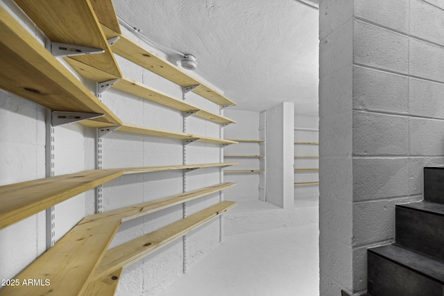 stairs featuring concrete block wall, a textured ceiling, and a wood stove