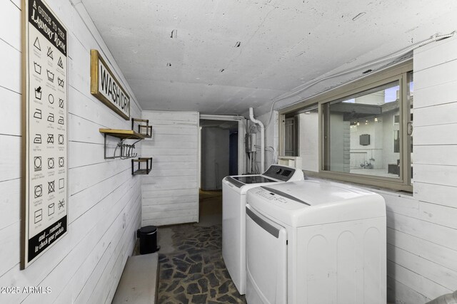 clothes washing area featuring separate washer and dryer and wood walls